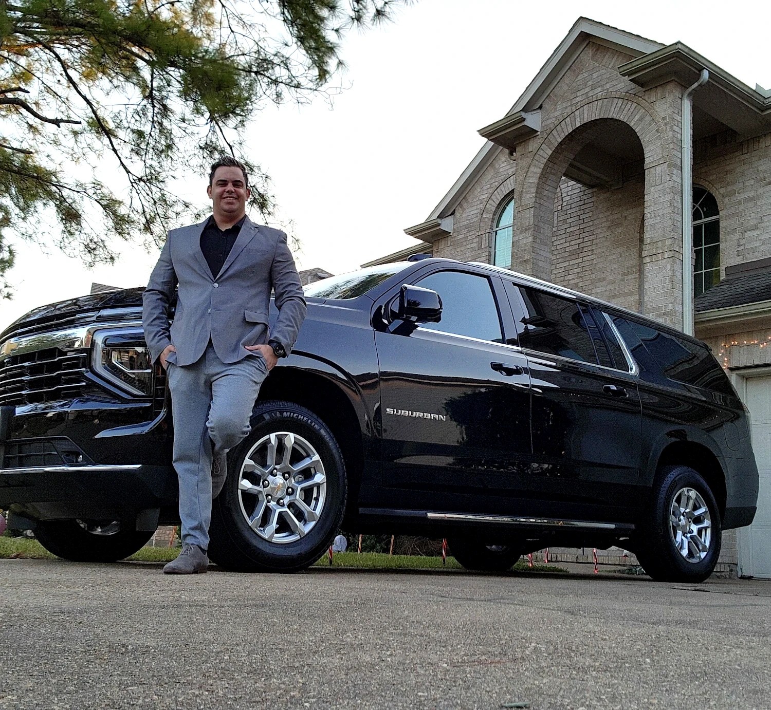 A chauffeur in a blue suit stands beside his luxurious black limousine.